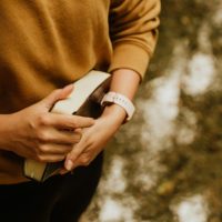 Woman holding Bible with a watch on. Bible Verses about pride and humility.