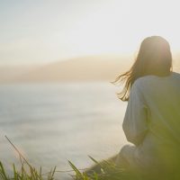 a woman sitting on a hill overlooking a body of water
